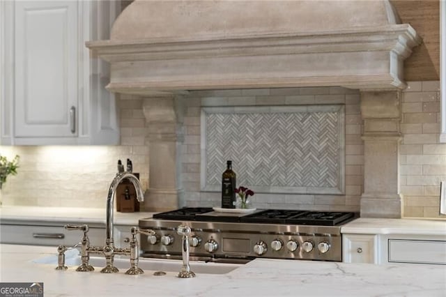 kitchen featuring custom exhaust hood, light stone counters, a tile fireplace, decorative backsplash, and white cabinets