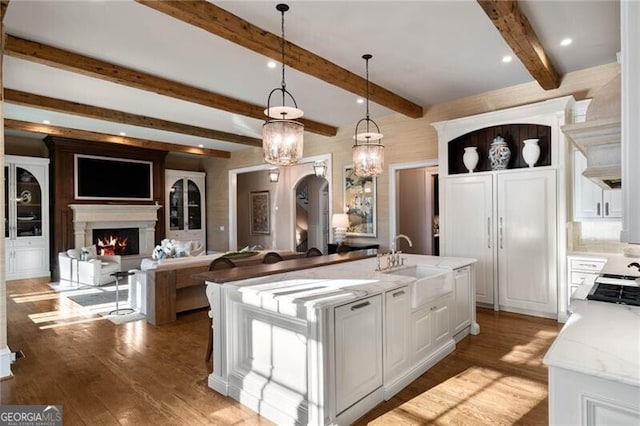 kitchen with sink, white cabinetry, hanging light fixtures, a kitchen island with sink, and light stone countertops