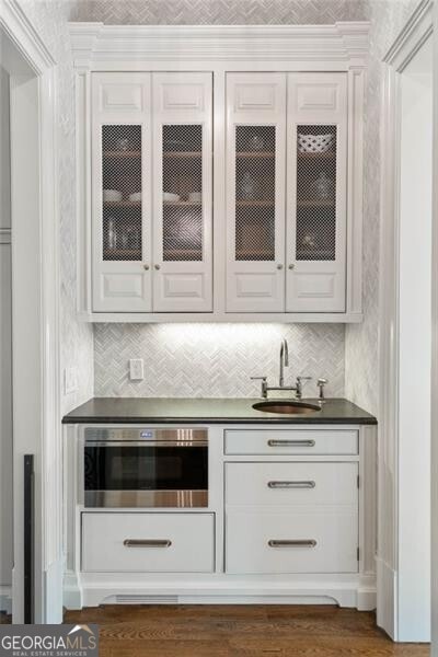 bar with white cabinetry, oven, and sink