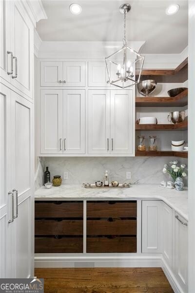 bar featuring dark wood-type flooring, hanging light fixtures, light stone countertops, white cabinets, and decorative backsplash