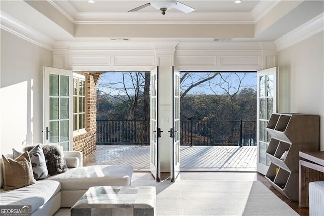 doorway with ornamental molding, a raised ceiling, and ceiling fan