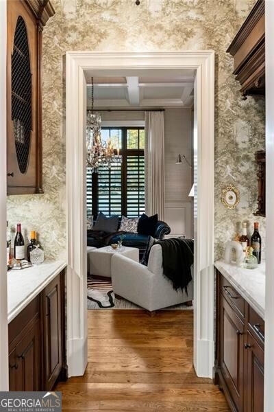 bar featuring dark brown cabinetry, ornamental molding, hardwood / wood-style floors, and a chandelier