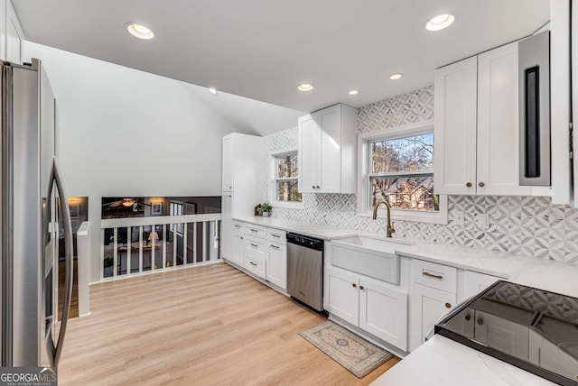 kitchen with sink, white cabinets, light stone counters, stainless steel appliances, and light hardwood / wood-style flooring