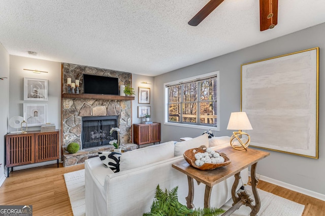 living room with ceiling fan, a fireplace, a textured ceiling, and light wood-type flooring