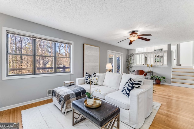 living room with french doors, ceiling fan, a textured ceiling, and light wood-type flooring