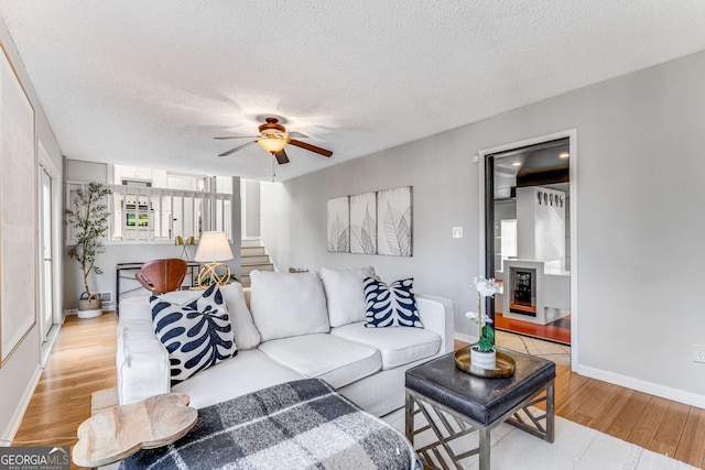 living room with ceiling fan, a textured ceiling, and light hardwood / wood-style flooring