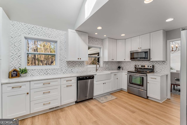 kitchen with appliances with stainless steel finishes, light hardwood / wood-style floors, sink, and white cabinets