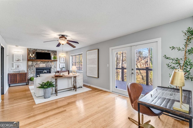 office space featuring french doors, a stone fireplace, light hardwood / wood-style floors, and a textured ceiling