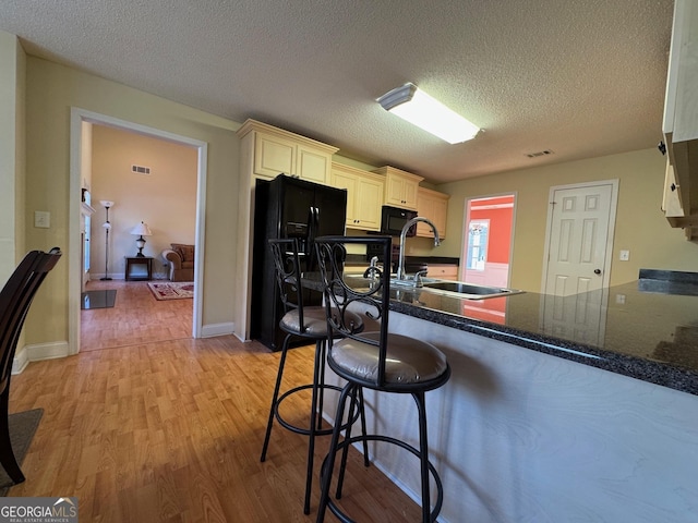 kitchen with black appliances, a textured ceiling, sink, light wood-type flooring, and kitchen peninsula