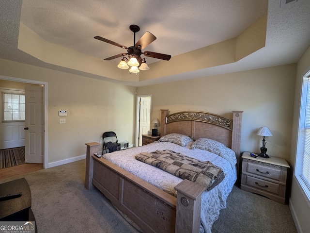 bedroom with ceiling fan, carpet flooring, a textured ceiling, and a tray ceiling