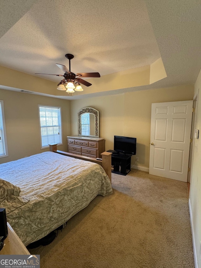 carpeted bedroom featuring ceiling fan, a textured ceiling, and a tray ceiling