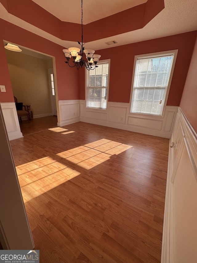 unfurnished dining area featuring a raised ceiling, a chandelier, and light wood-type flooring