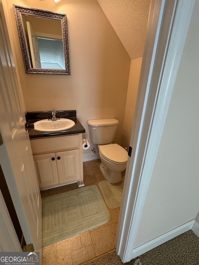 bathroom with toilet, a textured ceiling, lofted ceiling, and vanity