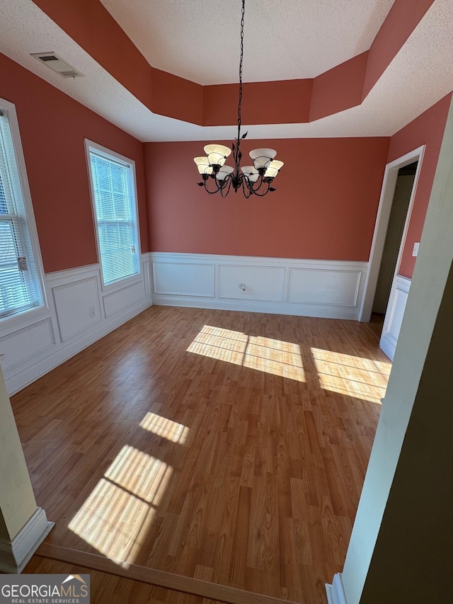 unfurnished dining area featuring a chandelier, a wealth of natural light, light hardwood / wood-style floors, and a textured ceiling