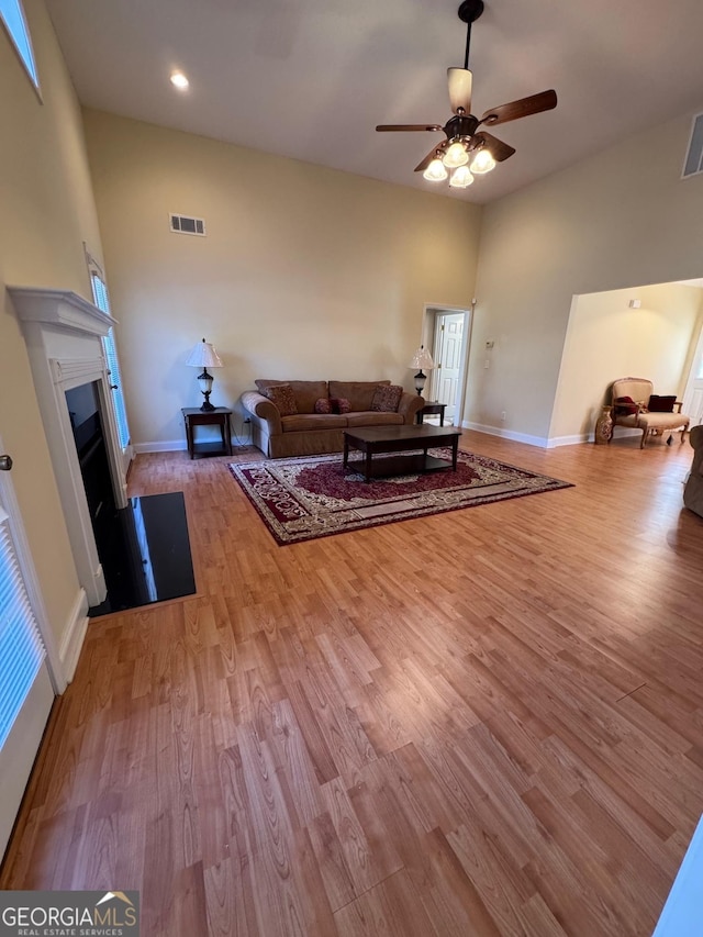 living room with ceiling fan, light hardwood / wood-style floors, and a towering ceiling