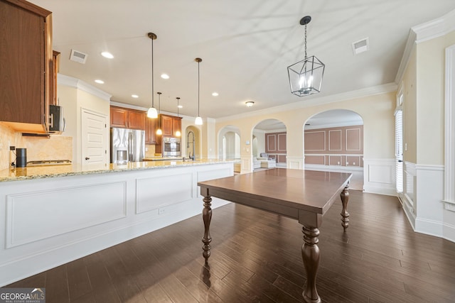 kitchen featuring stainless steel appliances, crown molding, light stone countertops, and decorative light fixtures