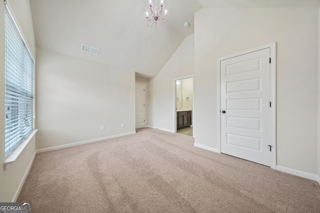 carpeted empty room with lofted ceiling and a notable chandelier