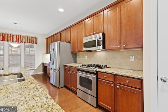 kitchen featuring light hardwood / wood-style floors, hanging light fixtures, sink, stainless steel appliances, and light stone counters