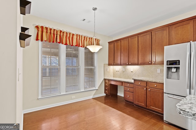 kitchen with built in desk, hanging light fixtures, hardwood / wood-style flooring, stainless steel fridge, and light stone counters