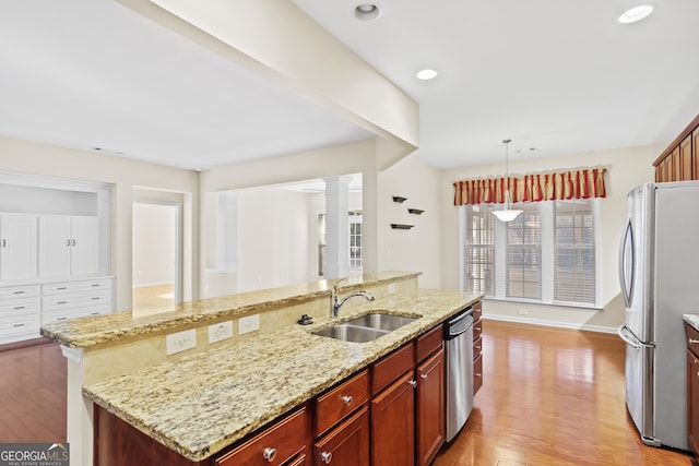 kitchen featuring hanging light fixtures, sink, light stone countertops, an island with sink, and stainless steel appliances