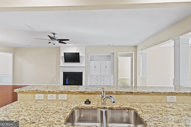 kitchen with sink, light stone countertops, hardwood / wood-style floors, a large fireplace, and decorative columns