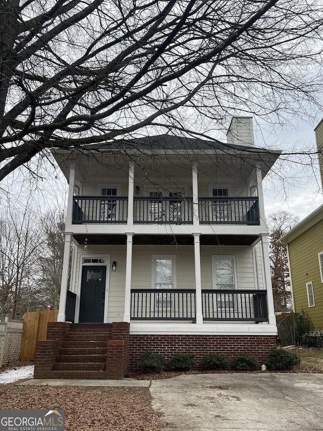 view of front of property with a porch, a chimney, a balcony, and fence