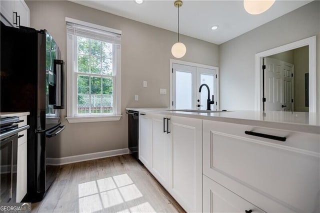 kitchen featuring baseboards, a sink, hanging light fixtures, white cabinetry, and light wood-type flooring