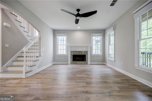 unfurnished living room featuring ceiling fan, a healthy amount of sunlight, light hardwood / wood-style flooring, and a tiled fireplace