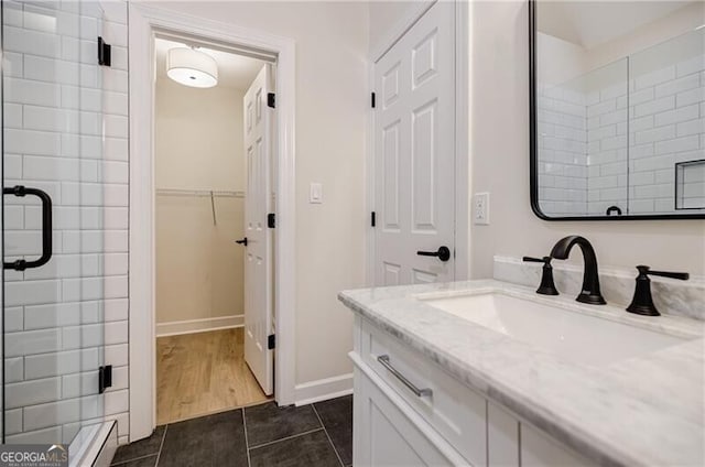 bathroom with a shower stall, tile patterned flooring, baseboards, a spacious closet, and vanity