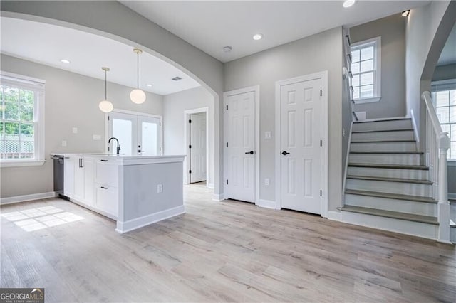 kitchen with white cabinets, light wood-style flooring, arched walkways, and a wealth of natural light