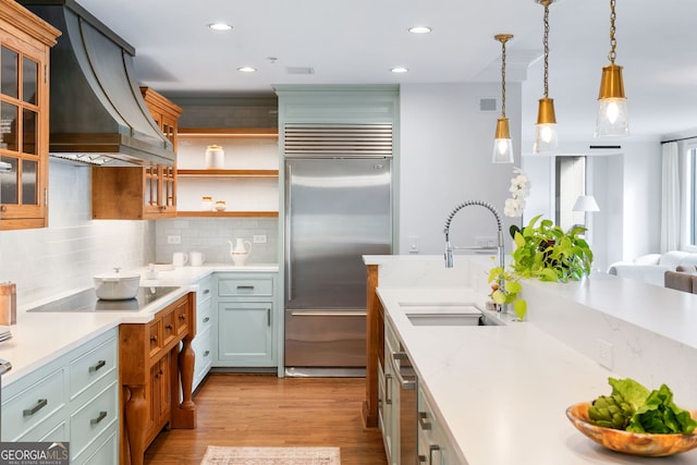 kitchen with black electric stovetop, built in fridge, a sink, custom exhaust hood, and pendant lighting