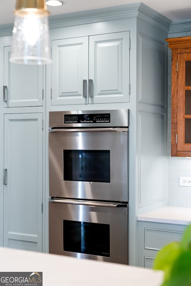 kitchen with light countertops, stainless steel double oven, white cabinetry, and crown molding