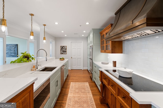 kitchen with decorative light fixtures, island exhaust hood, glass insert cabinets, appliances with stainless steel finishes, and a sink