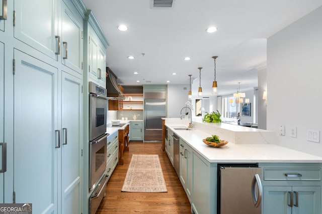 kitchen featuring appliances with stainless steel finishes, hanging light fixtures, a sink, and wood finished floors