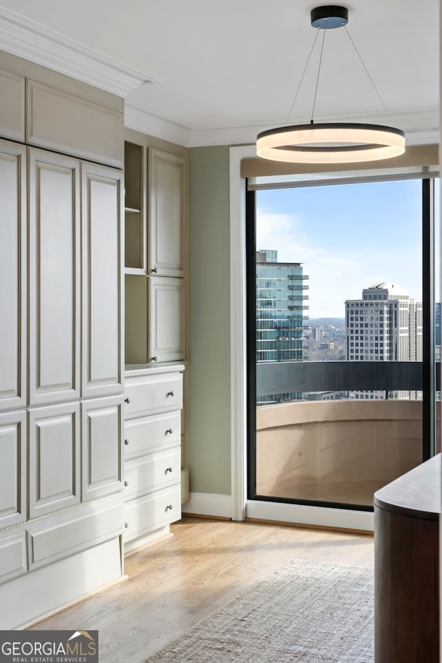 interior space with light wood finished floors, baseboards, a view of city, and ornamental molding