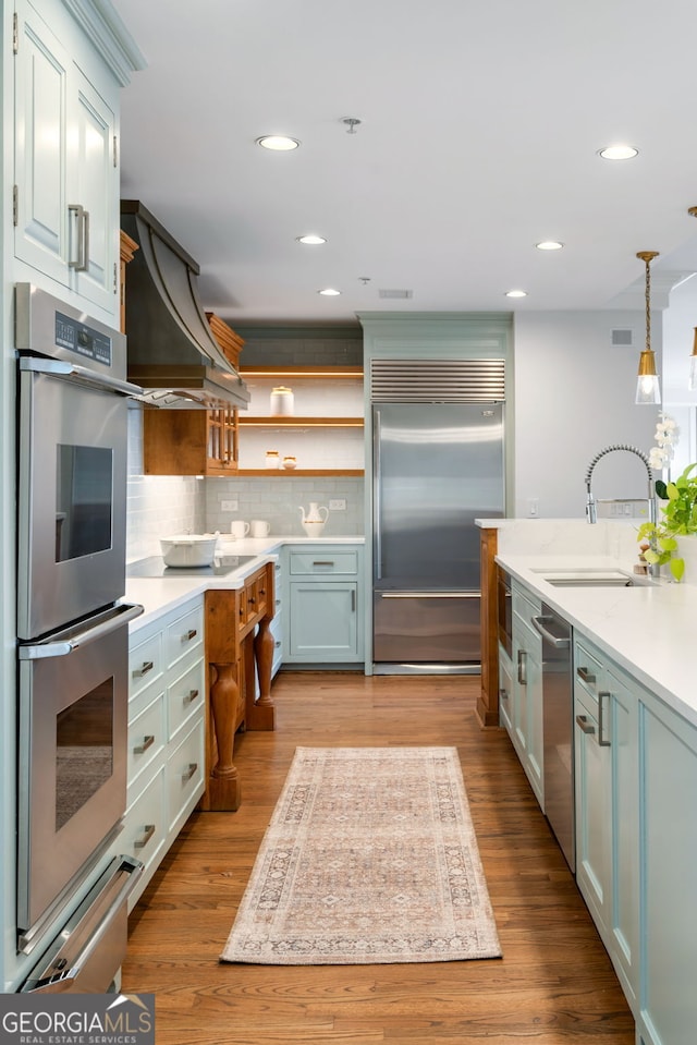 kitchen featuring appliances with stainless steel finishes, custom exhaust hood, light countertops, open shelves, and a sink