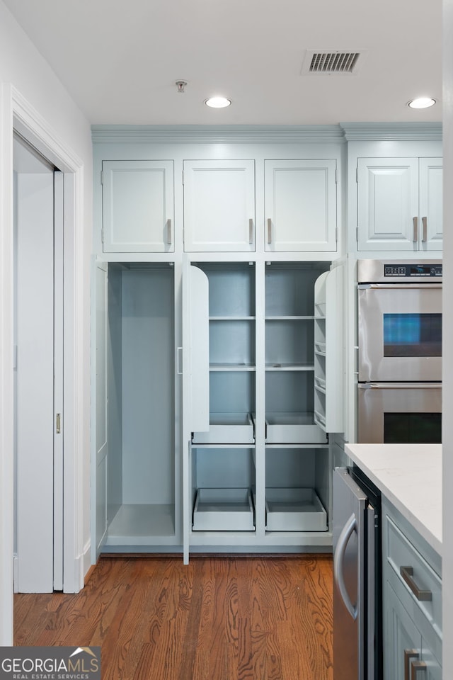 interior space with wine cooler, stainless steel double oven, visible vents, white cabinets, and light stone countertops