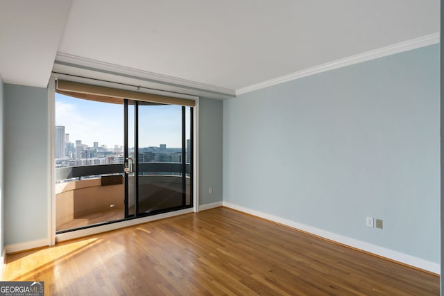 empty room with a view of city, crown molding, baseboards, and wood finished floors