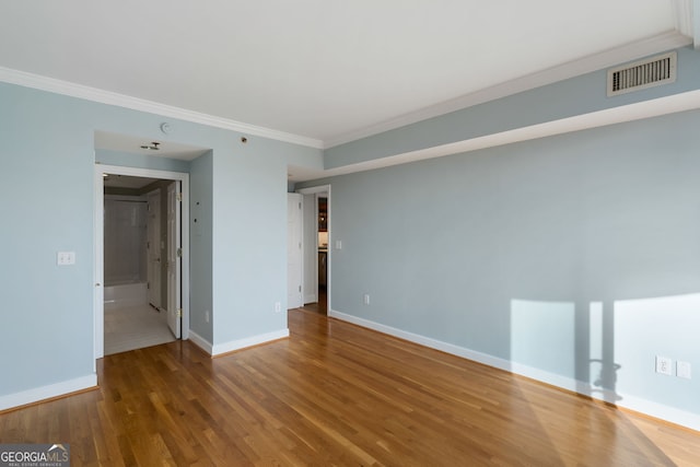 empty room featuring baseboards, crown molding, visible vents, and wood finished floors