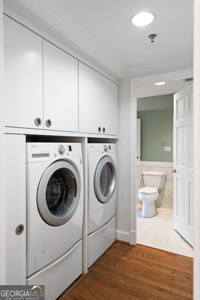 washroom featuring cabinet space, ornamental molding, wood finished floors, independent washer and dryer, and tile walls