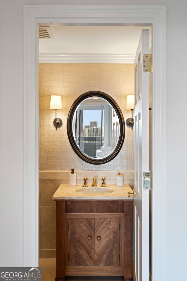 bathroom with visible vents, crown molding, vanity, and wallpapered walls