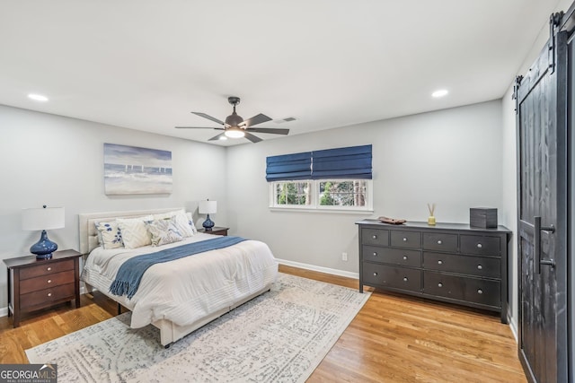 bedroom with ceiling fan, a barn door, and light wood-type flooring