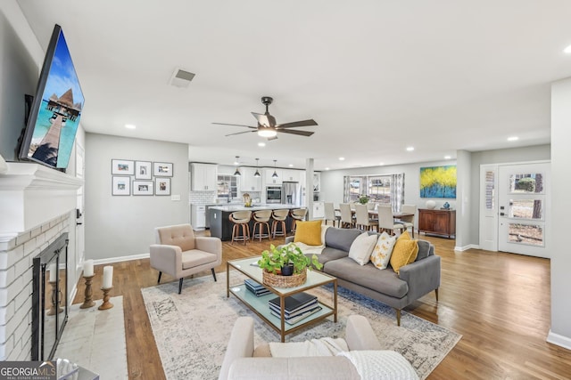 living room with ceiling fan, a brick fireplace, and light wood-type flooring