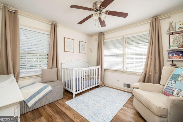 bedroom featuring crown molding, light wood-type flooring, ceiling fan, and a nursery area