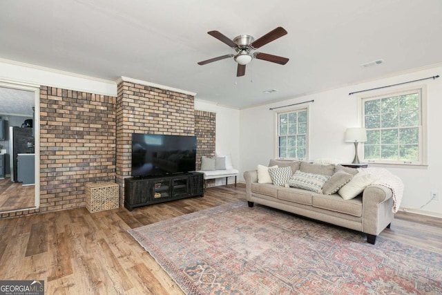 living room featuring hardwood / wood-style flooring, brick wall, ornamental molding, and ceiling fan