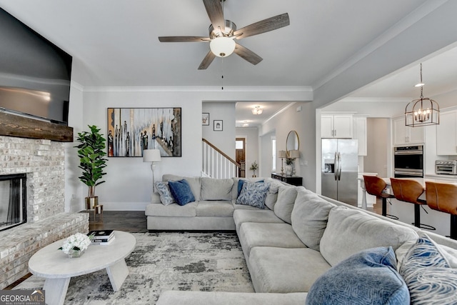 living room with ceiling fan with notable chandelier, ornamental molding, hardwood / wood-style floors, and a brick fireplace