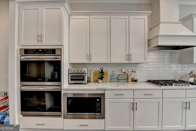 kitchen featuring backsplash, custom exhaust hood, stainless steel appliances, and white cabinets