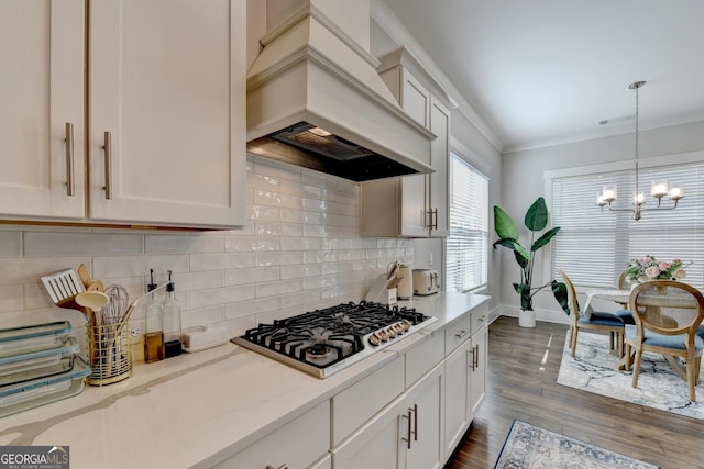 kitchen with pendant lighting, stainless steel gas cooktop, a notable chandelier, crown molding, and custom range hood