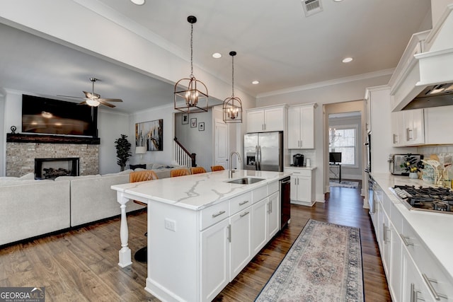 kitchen featuring sink, appliances with stainless steel finishes, white cabinetry, hanging light fixtures, and a center island with sink