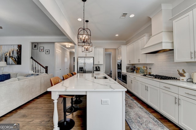 kitchen with sink, appliances with stainless steel finishes, a kitchen island with sink, custom range hood, and a kitchen bar